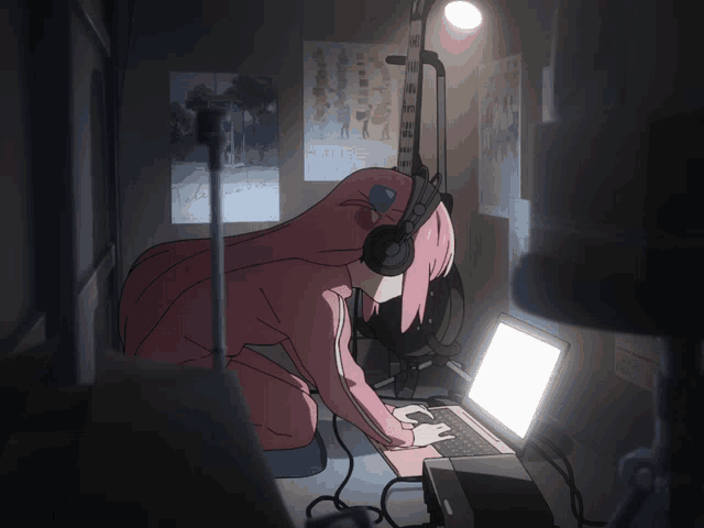 Bocchi hunched over a glowing laptop in a dark room, headphones on, typing away while her guitar leans on the wall behind her.